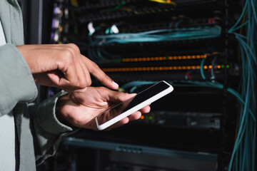cropped view of african american programmer pointing at smartphone with blank screen near server