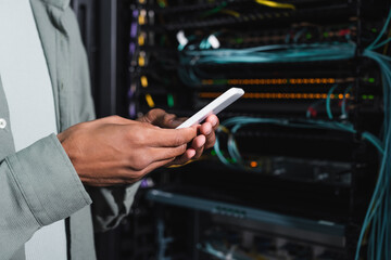 cropped view of african american engineer using smartphone near server in data center