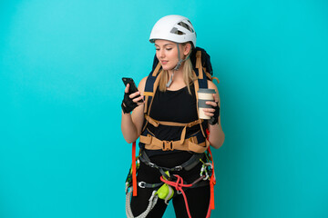 Young caucasian rock climber woman isolated on blue background holding coffee to take away and a mobile