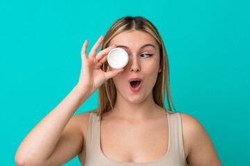 Young caucasian woman isolated on blue background with moisturizer and surprised