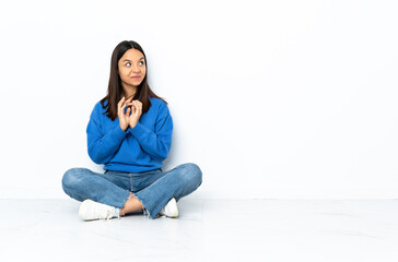 Young mixed race woman sitting on the floor isolated on white background scheming something