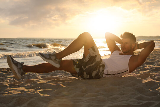 Sporty man with athletic body doing crunches on beach