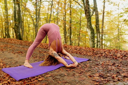 woman practicing yoga poses on purple mat in a forest during fall. meditation and healthy lifestyle.