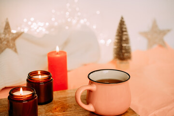 a cup with tea and three candles on a wooden table against a background with girlands. festive mood. merry christmas and happy new year.