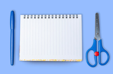 Notebook,pen and scissors isolated on blue background.Copy space