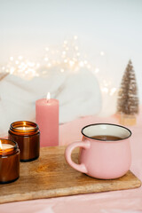 Obraz na płótnie Canvas a cup with tea and three candles on a wooden table against a background with garlands. festive mood. merry christmas and happy new year.