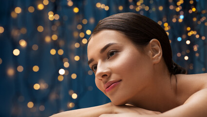 wellness, beauty and relaxation concept - young woman lying at spa or massage parlor over golden lights on blue background