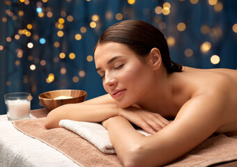 wellness, beauty and relaxation concept - young woman lying at spa or massage parlor over golden lights on blue background