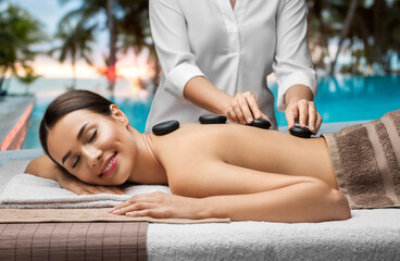 wellness, beauty and relaxation concept - beautiful young woman having hot stone massage at spa...