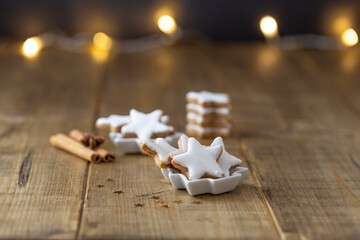 close-up of cinnamon stars as christmas cookies in a little white bowl on a wooden table, focus on foreground, bokeh in the background