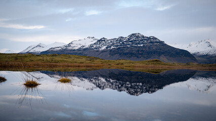 Mountains are reflected in the placid waters around lava fields crossed by a road in East Iceland...