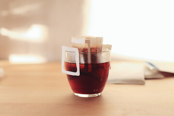 A coffee glass with drip bag on a wooden table