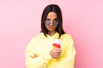 Young brunette girl holding a cornet ice cream over isolated pink background feeling upset