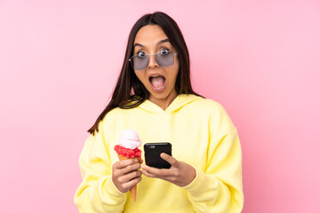 Young brunette girl holding a cornet ice cream over isolated pink background surprised and sending a message