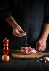 Chef sprinkles the meat with salt. Preparing meat before baking. Working environment in restaurant kitchen.
