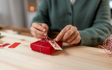 winter holidays and hobby concept - close up of woman with box and rope packing christmas gift or making advent calendar at home