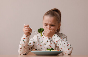 Cute little girl covering mouth and refusing to eat her dinner at table on grey background