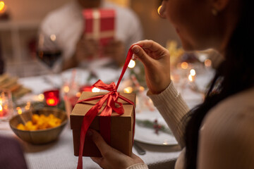 winter holidays and celebration concept - close up of happy woman opening christmas gifts at home dinner party