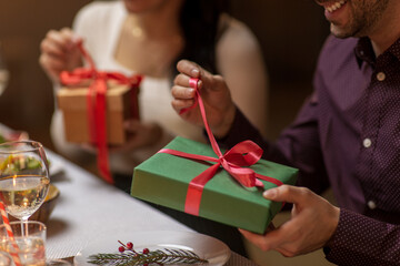 winter holidays and celebration concept - close up of happy smiling people opening christmas gifts at home dinner party