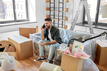 moving, people and real estate concept - happy smiling man with boxes calling on smartphone at new home