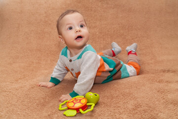 Portrait of a baby with big eyes lying on his stomach on a beige neutral background.