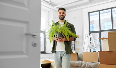 moving, people and real estate concept - happy smiling man with fern flower at new home
