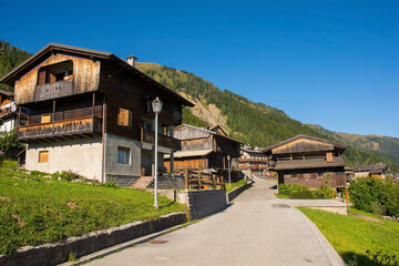 Fototapeta na wymiar A road of traditional wooden buildings in the Alpine village of Sauris di Sopra, Udine Province, Friuli-Venezia Giulia, north east Italy. Monte Morgenleit is in the background 