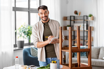 furniture renovation, diy and home improvement concept - man with old wooden table writing to notebook