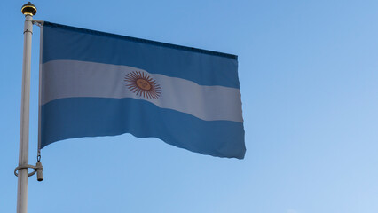 National flag of Argentina on a flagpole in front of blue sky with sun rays and lens flare. Diplomacy concept.
