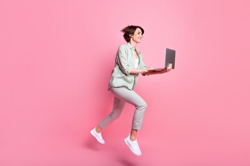 Fototapeta na wymiar Full length profile photo of nice millennial lady jump with laptop wear grey green suit isolated on pink color background