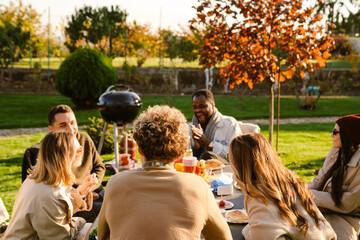 Multiracial friends talking and laughing during barbeque in garden