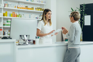 Female pharmacist selling medications at drugstore to a senior woman customer