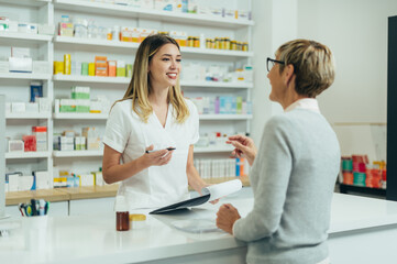 Happy senior woman customer buying medications at drugstore while talking with a female pharmacist