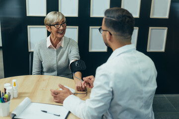 Fototapeta premium Smiling senior woman patient in doctor's office checking blood pressure