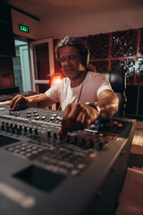 Senior hispanic music producer working on a mixing soundboard while in his studio