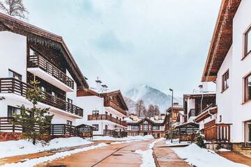 Cozy wooden cottages in chalet style covered with snow. Beautiful snowcapped mountain peak. Xmas...