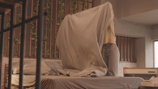 Slowmo shot of young Asian woman laying blanket while making bed doing housework at modern apartment