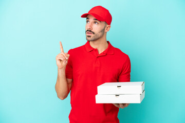 Delivery caucasian man picking up pizza boxes isolated on blue background thinking an idea pointing...