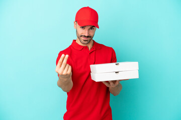 Delivery caucasian man picking up pizza boxes isolated on blue background making money gesture