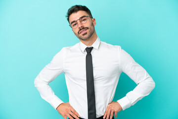 Business caucasian man isolated on blue background posing with arms at hip and smiling