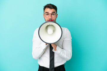 Business caucasian man isolated on blue background shouting through a megaphone