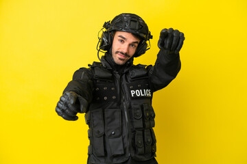 SWAT caucasian man isolated on yellow background points finger at you while smiling