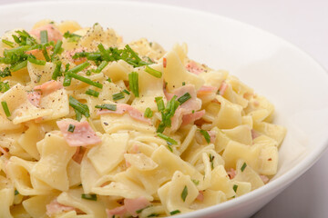 Closeup of the Traditional Austrian Dish so called Schinkenfleckerl on a white plate with red and white background