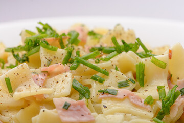 Closeup of the Traditional Austrian Dish so called Schinkenfleckerl on a white plate with red and white background