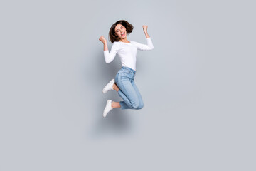 Fototapeta premium Photo of impressed lucky young woman wear white outfit jumping high rising fists smiling isolated grey color background