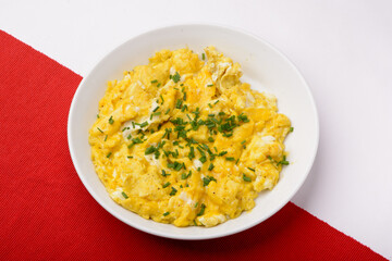 scrambled breakfast eggs on a white plate with red and white background