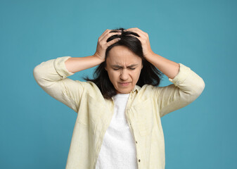 Mature woman suffering from headache on light blue background