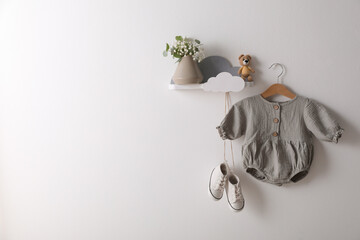 Cute baby onesie and shoes hanging on white wall. Space for text