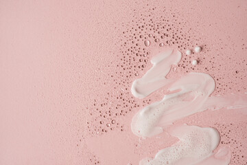 Beauty, skincare products setting. White cosmetic cream smear on neutral pink background. White beauty foam, powder