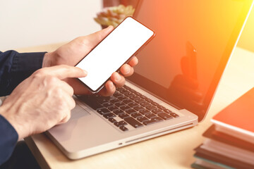 Phone and laptop in hand on the desktop in the office or at home. Smartphone blank screen mockup. Using web, shop, apps concept.